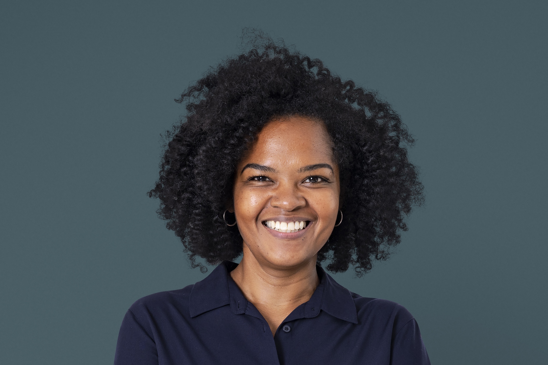 A professional headshot of a woman smiling wearing a navy blue shirt collared shirt.