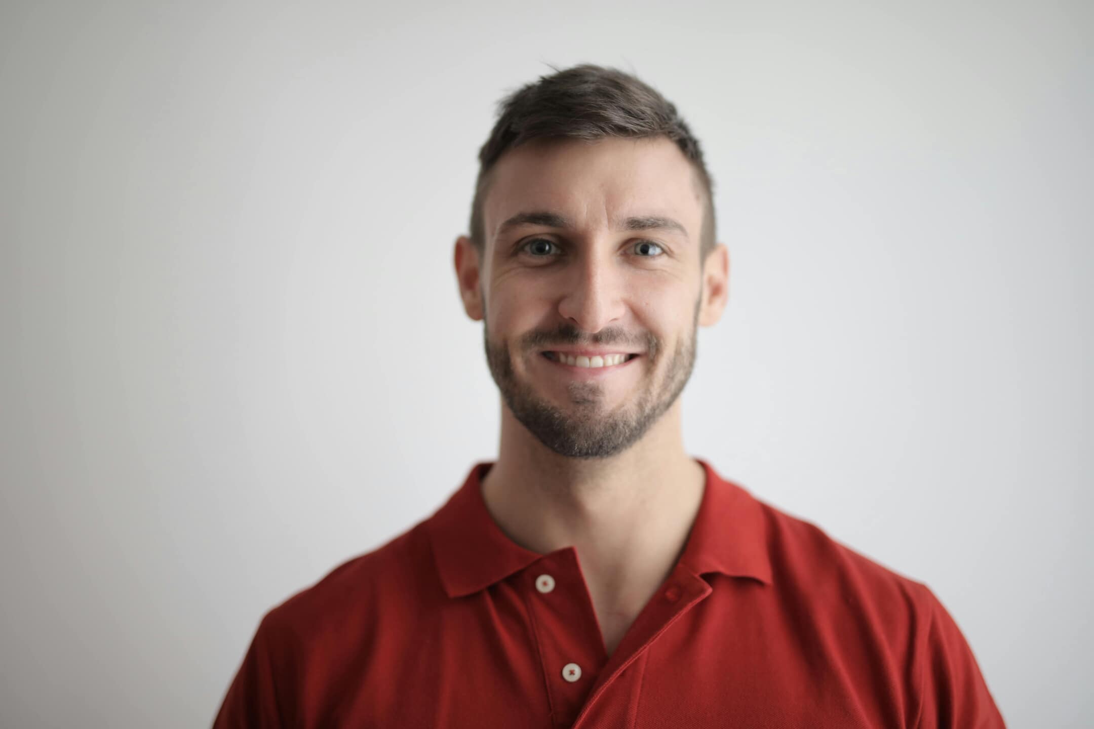 A professional headshot of a man smiling wearing a red polo.